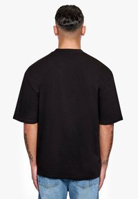 Black cotton T-shirt with short sleeves, a crew neck, and a relaxed fit. Back view shows minimal detailing and textured fabric.