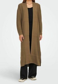 Cardigan long ouvert en tricot texturé de couleur vert olive. Doté de manches côtelées, d'échancrures latérales et d'une coupe décontractée. Associé à un haut et un pantalon noirs.