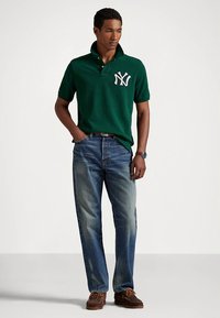 Grønn poloshirt med NY-logo, falmede blå jeans og brune loafers. Kortermet, klassisk passform, glat stoff og synlige sømmer.
