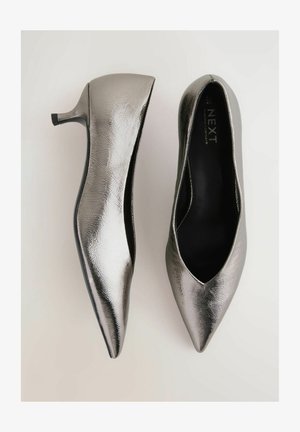 Scarpe con tacco alto in metallo argentato, con punta affusolata e texture liscia, che presentano un design slip-on e un tacco basso.