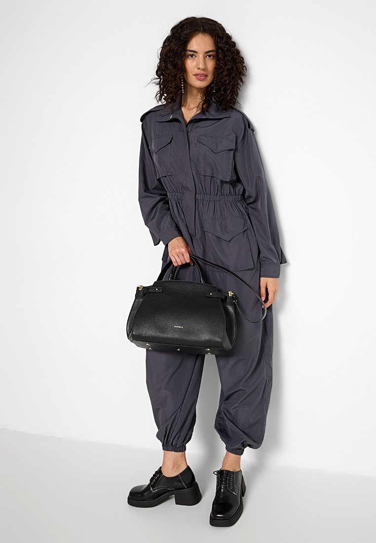 Szary kombinezon z przednimi kieszeniami i elastycznym pasem, w połączeniu z czarną torebką o teksturowanej powierzchni i czarnymi sznurówkami. Prosty i funkcjonalny design.