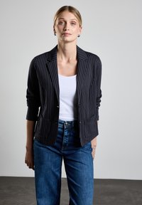 Svart rutigt blazer med skräddarsydd passform, med långa ärmar, två framfickor och en slagkrage, matchat med en vit topp och blå jeans.