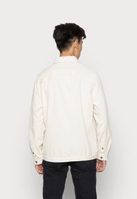 Light beige corduroy jacket with a collar, long sleeves, and buttoned cuffs. Features vertical ridges and a straight cut design.