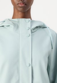Lys blå hettegenser med trykknapper, en glatt tekstur, justerbar snøring og et minimalistisk design.