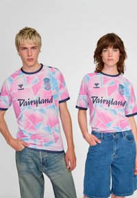 Zwei Personen tragen passende pastellfarbene Trikots mit einem geometrischen Muster in Pink und Blau, schwarzem Besatz und dem Text "Dairyland".