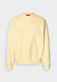 Sweat-shirt jaune clair à col rond avec manches longues et texte « HUGO » subtilement en relief sur la poitrine.