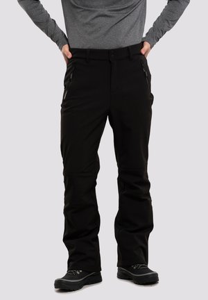 Zwarte softshell broek met ritszakken, een rechte pasvorm en verstevigde knieën, gecombineerd met stevige zwarte wandelschoenen.