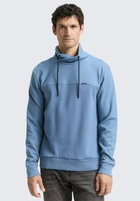 Sweat-shirt à col montant bleu clair avec cordon de serrage et panneau contrastant bleu plus foncé sur la poitrine. Texture de tissu douce.