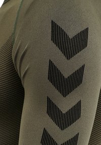 Olivgrön topp i texturerat tyg med vertikala ränder. Svart chevronmönster längs axeln ger kontrast och detalj.