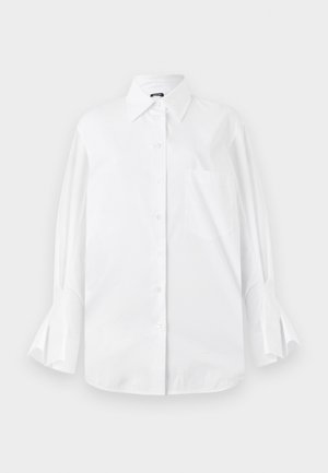 Camicia bianca con bottoni, realizzata in cotone, con colletto classico, maniche lunghe e polsini svasati. Presenta una tasca sul petto. Texture liscia.