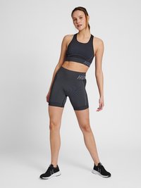 Schwarzer sportlicher Sport-BH und Shorts mit gerippter Textur, Logodetail und figurnahem Design. Kombiniert mit schwarzen Sportschuhen.