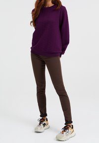 Violetti teksturoitu neulepaita pitkillä hihoilla, yhdistettynä tiukkoihin ruskeisiin housuihin ja monivärisiin lenkkareihin, joissa on paksu pohja.