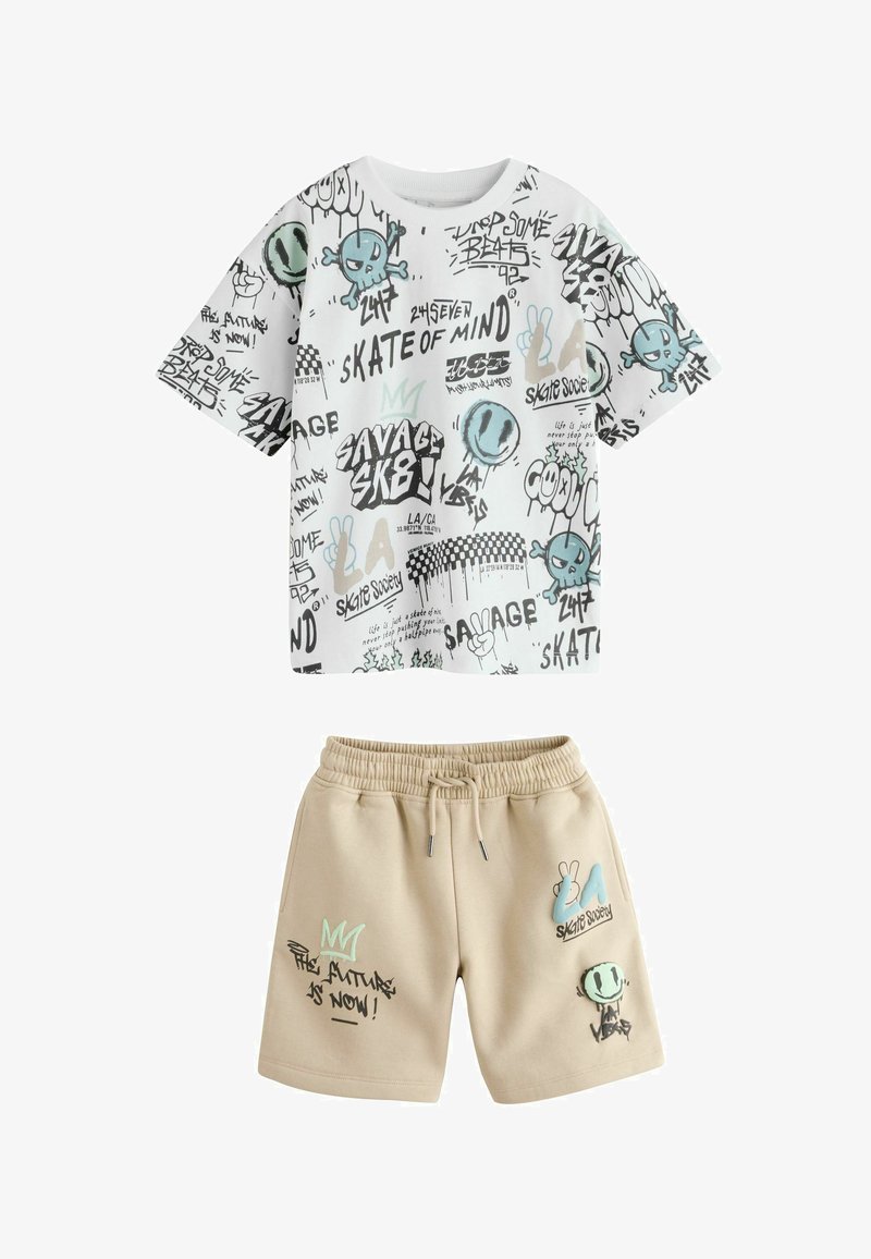 Witte kortärmelig blouse en beige korte broek met graffiti-stijl tekst en blauw- en groenachtige grafische ontwerpen, inclusief schedels en smiley gezichten.