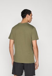 Κοντομάνικο μπλουζάκι σε ελιά πράσινο με στρογγυλή λαιμόκοψη, κατασκευασμένο από μαλακό ύφασμα. Εφαρμοστό σχέδιο, με ελάχιστες λεπτομέρειες, συνδυασμένο με μαύρο σορτς.