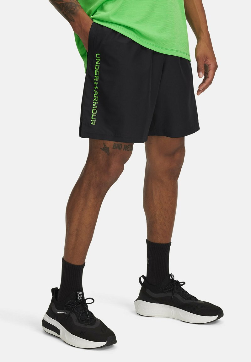 Juodi sportiniai šortai iš lengvo audinio, su žaliu "UNDER ARMOUR" logotipu kairėje pusėje. Nešiojami su juodais sportiniais batais ir kojinėmis.