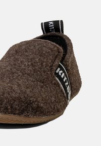 Pantofola in feltro marrone con punta arrotondata, suola in cuoio e una fascia nera con la scritta “Kitzbühel.” Texture morbida con un design semplice.