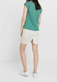 Vihreäraitaista lyhythihaista puseroa yhdistettynä beigeen, polven mittaiseen hameeseen, jossa on takana halkio. Käytetty valkoisten tennareiden kanssa.