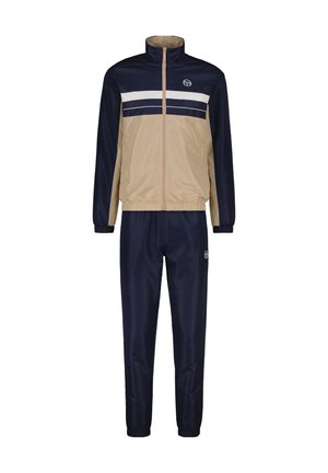 Tuta navy e beige con giacca con zip caratterizzata da strisce orizzontali bianche e pantaloni coordinati. Realizzato in materiale liscio e leggero.