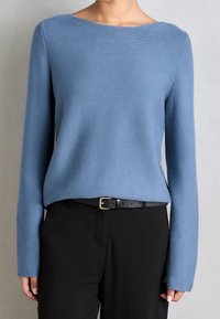 Maglione a maglia azzurro chiaro con scollo a barca, maniche lunghe e vestibilità rilassata, abbinato a pantaloni neri e una cintura nera con fibbia argento.