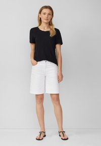 Zwarte T-shirt met korte mouwen, witte denim shorts met opgerolde mouwen en zwarte sandalen. Eenvoudige, casual outfit met contrasterende kleuren.