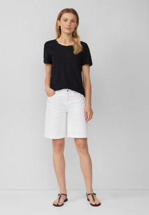 Chemise noire à manches courtes, shorts en denim blancs avec ourlets retroussés, et sandales noires. Tenue simple et décontractée avec des couleurs contrastées.