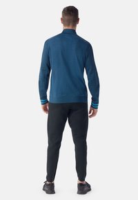 Maglia blu a maniche lunghe da uomo con un motivo testurizzato, polsini a costine e righe a contrasto. Abbinata a pantaloni neri a gamba stretta e sneakers.