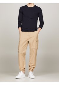 Navy long-sleeve t-shirt with a small logo, paired with khaki cargo pants featuring side pockets and elastic cuffs, completed with white sneakers.