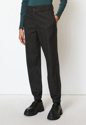 Person wearing dark gray checkered pants with elastic cuffs, green long-sleeve top, and black chunky platform shoes.