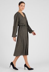 Abito di lunghezza media in nero con fili scintillanti e multicolori. Presenta un colletto a V, maniche a sbuffo e una vita cinte per un look aderente.