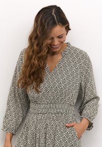 Haljina s crno-bijelim uzorkom, V-izrezom, balon rukavima i elastičnom strukom. Sadrži cvjetne motive i bočne džepove.