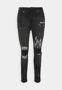 Black denim jeans with distressed knees, featuring white graphic prints, splatter patterns, and a drawstring waist.