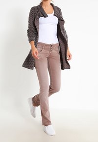 Cardigan largo de patrón marrón sobre una blusa blanca, combinado con jeans ajustados de color marrón claro y zapatillas blancas, creando un atuendo casual.