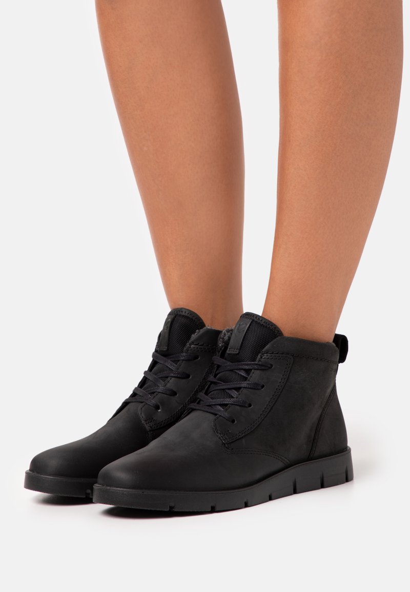 Botas de tobillo negras de cuero, con un diseño de cordones, superficie texturizada y una suela de goma baja y resistente.