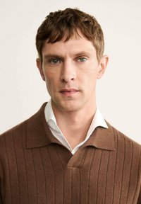 Maglione a coste marrone con scollatura a V e colletto corto, indossato sopra una camicia bianca, caratterizzato da una texture liscia e dettagli sottili.