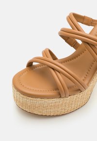 Sandalias de plataforma de cuero marrón con tiras entrecruzadas, plantilla acolchada y una entresuela de yute trenzado para aportar textura y detalle.