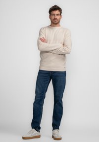 Beige gestreepte pullover trui met ronde hals, gecombineerd met donkerblauwe spijkerbroek en lichte sneakers, in een comfortabele pasvorm.