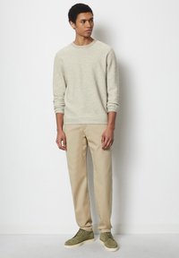 Hellgrauer strukturierter Sweatshirt mit gerippten Bündchen, kombiniert mit beigen Hosen und grünen Wildlederschuhen. Das Modell steht vor einem schlichten Hintergrund.