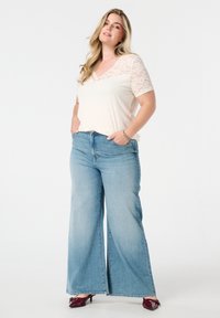 Lichtbeige top met kant korte mouwen, gecombineerd met lichtblauwe wijde jeans. De outfit heeft een relaxte pasvorm en een subtiel textuurcontrast.