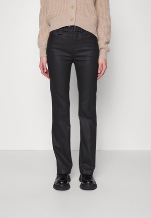 Pantalons slim noirs avec une texture lisse, dotés d'une taille mi-haute, d'un léger brillant et de poches latérales, associés à des chaussures noires chunky.