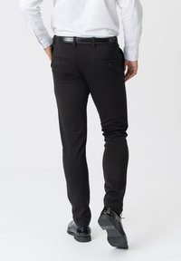 Sorte slim-fit bukser med baglommmer, glat tekstur og skræddersyet design. Matchet med blanke sorte sko, som viser hæl og sål.