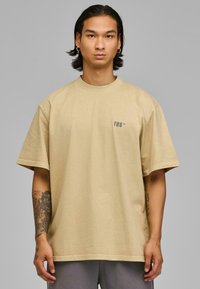 Tricou oversized bej cu mâneci scurte, având un mic logo gri în zona stângă a pieptului. Material din bumbac moale, croială lejera.
