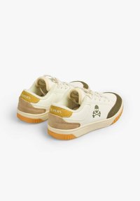 Sneaker mit einem Obermaterial aus cremefarbenem Canvas, olivgrünen Akzenten, einem beigen Wildleder-Fersenbereich und einem gelben Etikett; mit einem Totenkopf-Logo und einer Gummisohle.