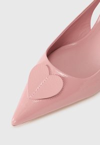 Ροζ γυαλιστερό δερμάτινο παπούτσι με μυτερή μύτη και καρδιόσχημο διακοσμητικό στην επάνω πλευρ ά. Λείο υλικό και κομψός σχεδιασμός χωρίς ορατά εξαρτήματα.