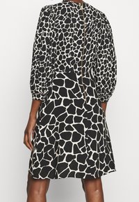 Svart och vit klänning med giraffmönster, puffärmar och en synlig guldkedja bak. A-linjeformad siluett, knälång design.