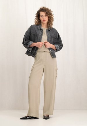 Donkergrijze oversized spijkerjack, beige cargobroek met elastische tailleband, soepele textuur, ronde zwarte versieringen op schoenen.