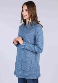 Blaue gemusterte Tunika mit hohem Kragen, die ein sich wiederholendes Blattmotiv aufweist, lange Ärmel, zwei Fronttaschen und gestreifte Akzente an den Bündchen.