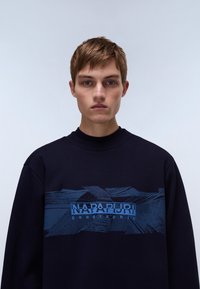 Navy sweatshirt van katoen, met een textuur blauw grafisch ontwerp over de borst met de tekst "NAPAPIJRI geographic". Ronde halslijn.