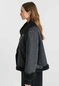 Giacca di jeans nera con colletto in shearling, vestibilità oversized, polsini a coste e tasche laterali. Tessuto texturizzato con un morbido rivestimento interno.