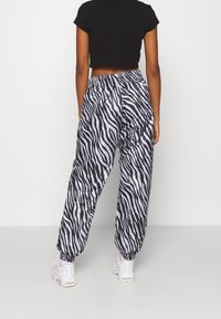 Černé zkrácené tričko skombinované s volnými kalhotami se zebra vzorem v šedé a černé barvě. Kalhoty mají elastický pás a manžety.