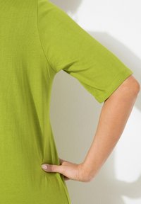 Top a maniche corte di colore verde lime realizzato in tessuto liscio, con scollatura a girocollo e silhouette aderente. Dettaglio di cucitura discreta sulle maniche.